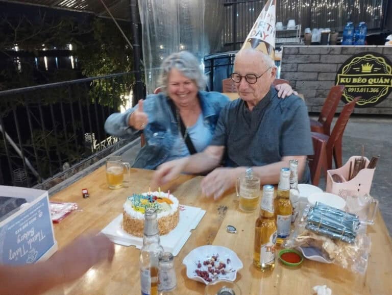 Deux personnes souriantes lors d'une fête d'anniversaire avec gâteau et boissons.