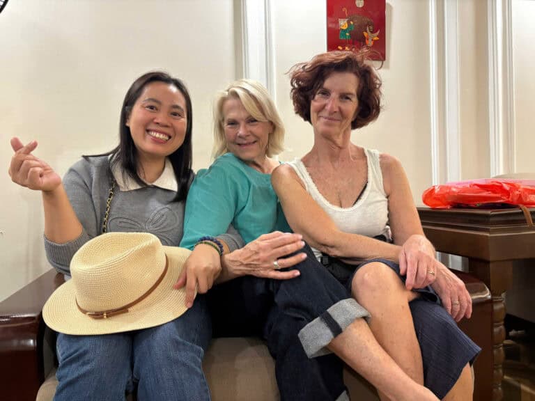 Trois femmes souriantes assises, partageant un moment convivial, représentant l'accueil chaleureux e.