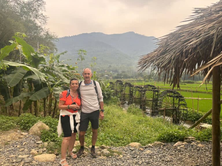 Voyageurs devant un paysage rural vietnamien avec rizières et montagnes.