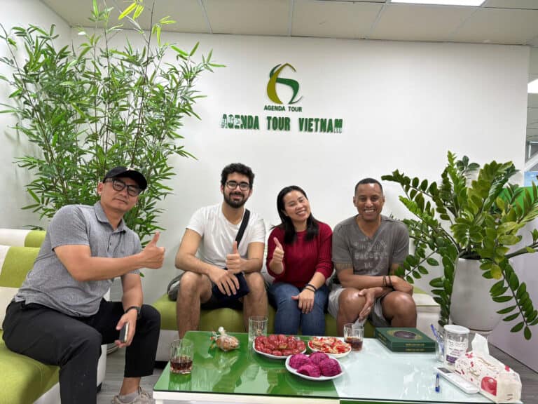 Voyageurs souriants avec logo Agenda Tour Vietnam, assis dans un espace moderne avec plantes vertes,.