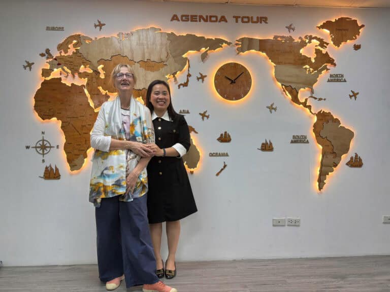Deux femmes souriantes devant une carte du monde lumineuse à l'agence Agenda Tour Vietnam.