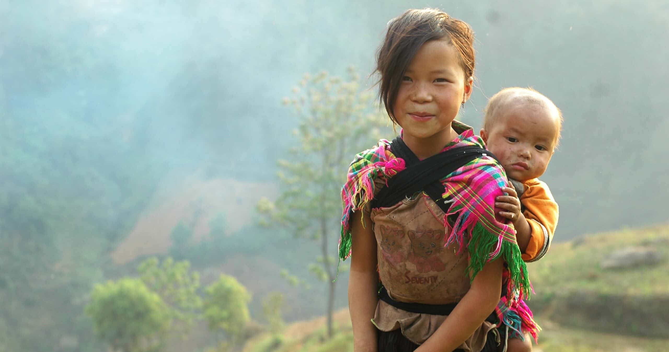 Jeune fille souriante portant un bébé dans un environnement rural verdoyant.